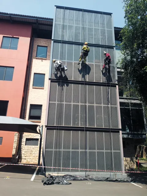 Three MP technicians on ropes painting a perforated steel facade