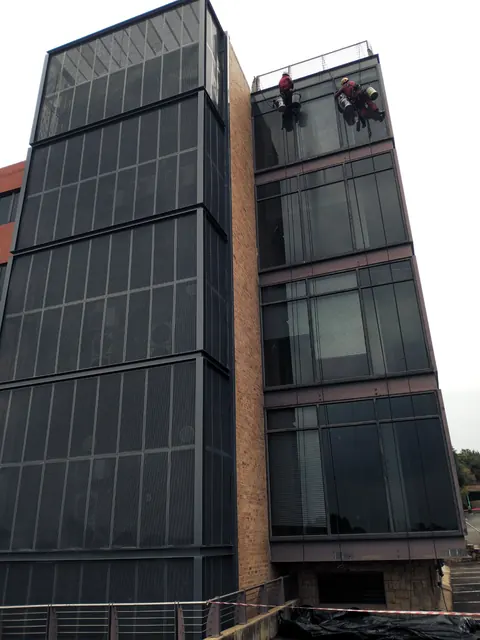 Two MP technicians on ropes at the roofline of a glass and steel office block
