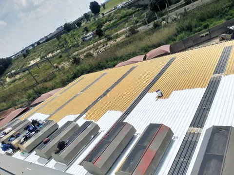Factory roof part-way through coating, gold primer and white top coat, with the city behind