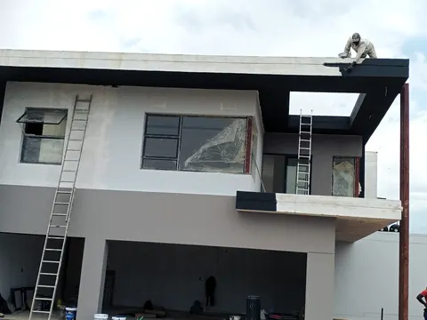 Painter on the roof edge finishing the fascia of a new double-storey house