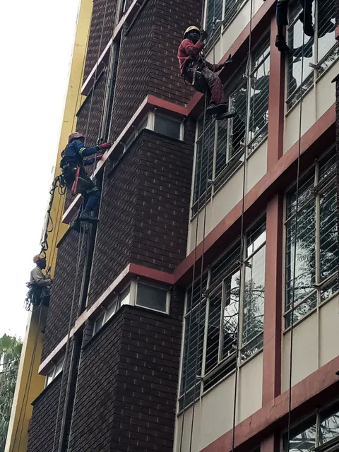 Four MP technicians on ropes working down a brick and plaster high-rise