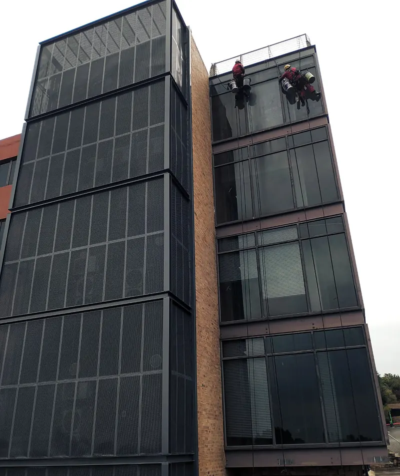 Two MP technicians on ropes at the roofline of a glass and steel office block
