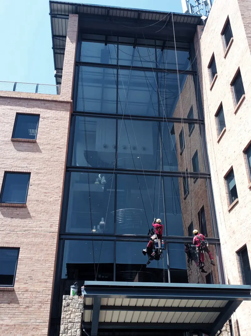 Two MP technicians working on a glass curtain wall above an entrance canopy